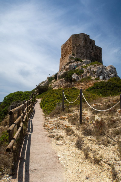 Castillo de Cabrera sobre un promontorio rocoso, con el sendero de subida y vegetación mediterránea, en el Parque Nacional de Cabrera