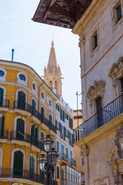 Calle del casco antiguo de Palma, con edificios señoriales de fachada ocre, balcones de hierro y un campanario gótico al fondo